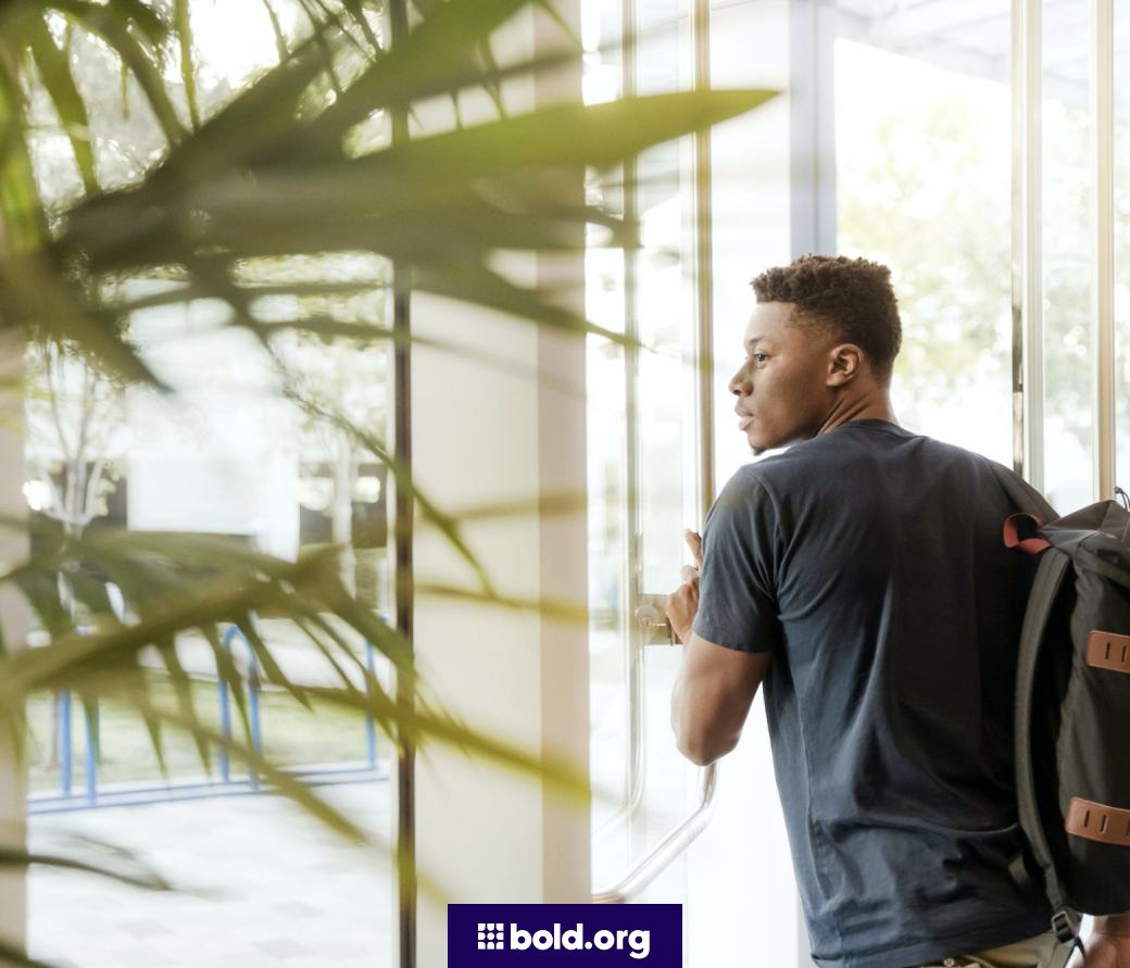 Student with a backpack walking through a glass door