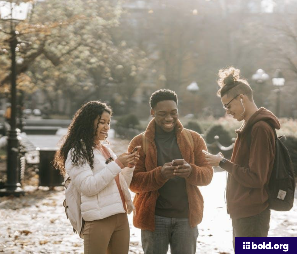 Three students laughing on their phones outside