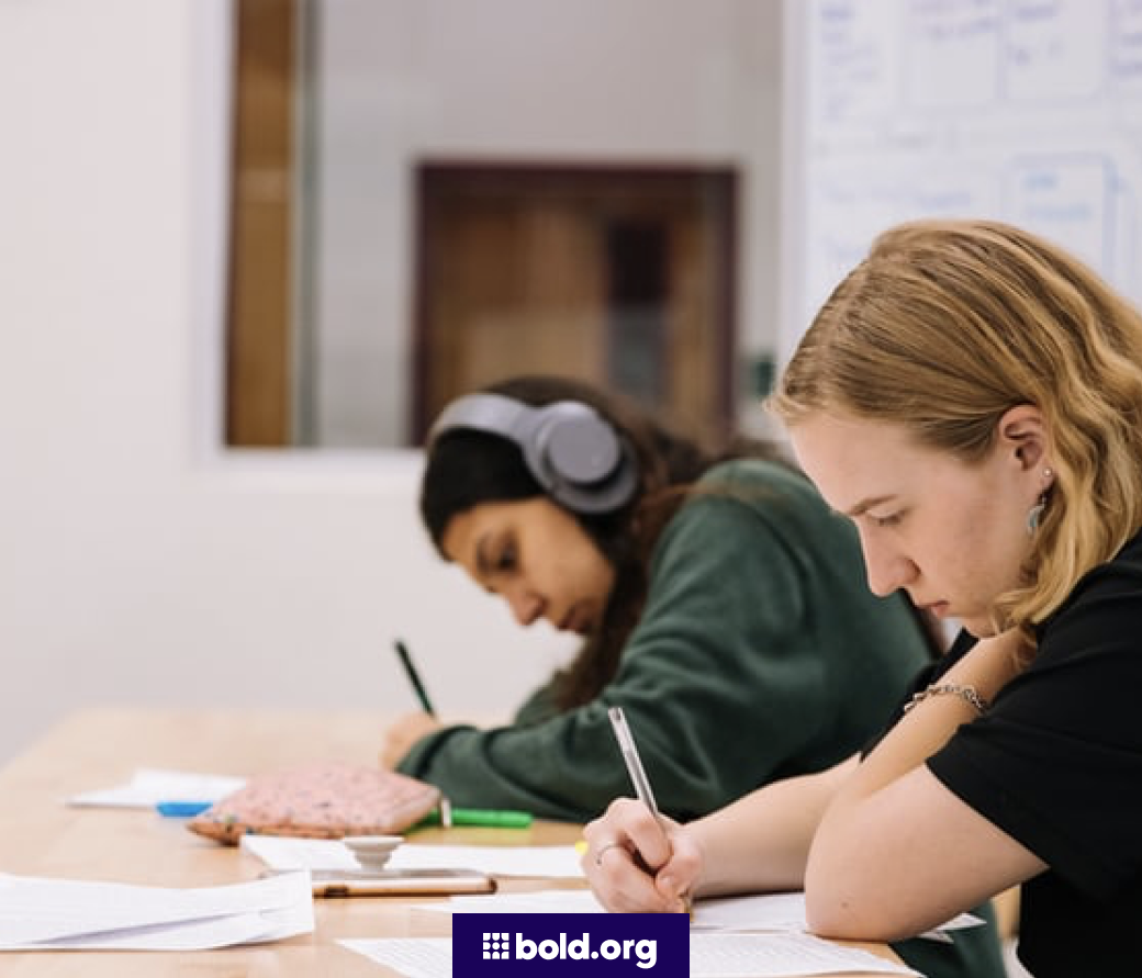 Two female students taking notes at a table