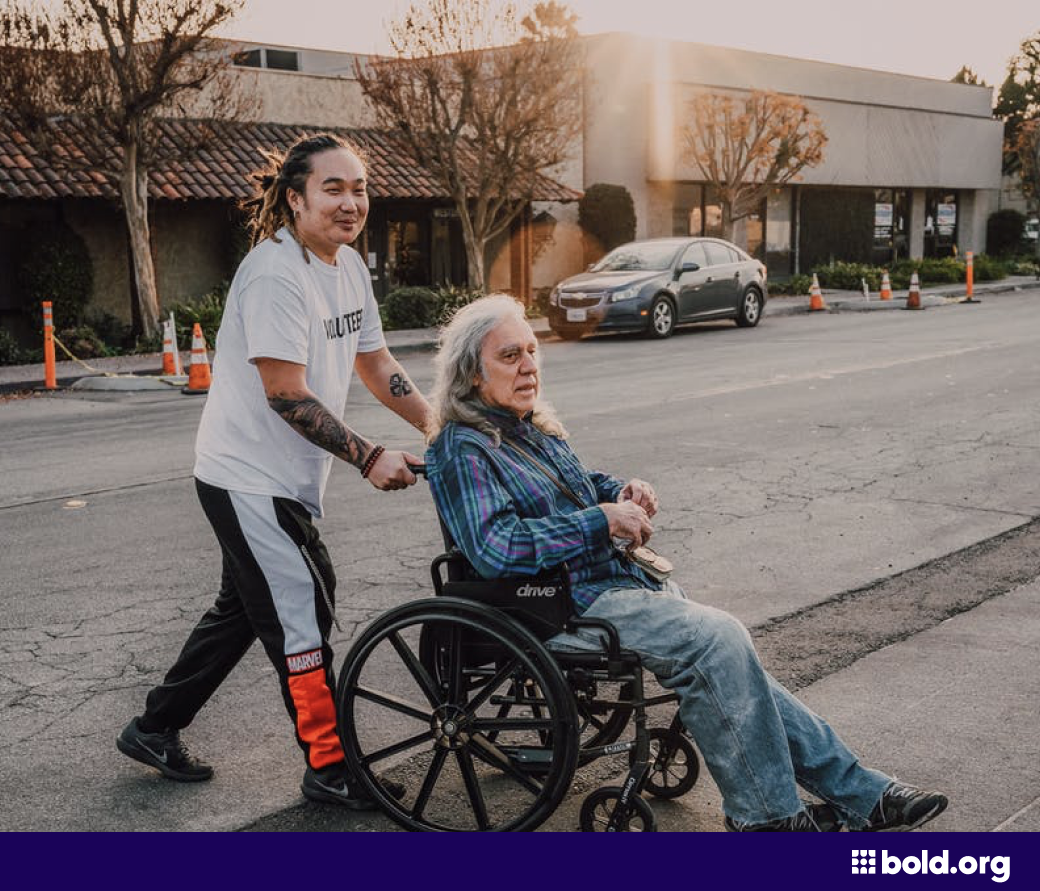 Volunteer helping a man in a wheelchair cross the street