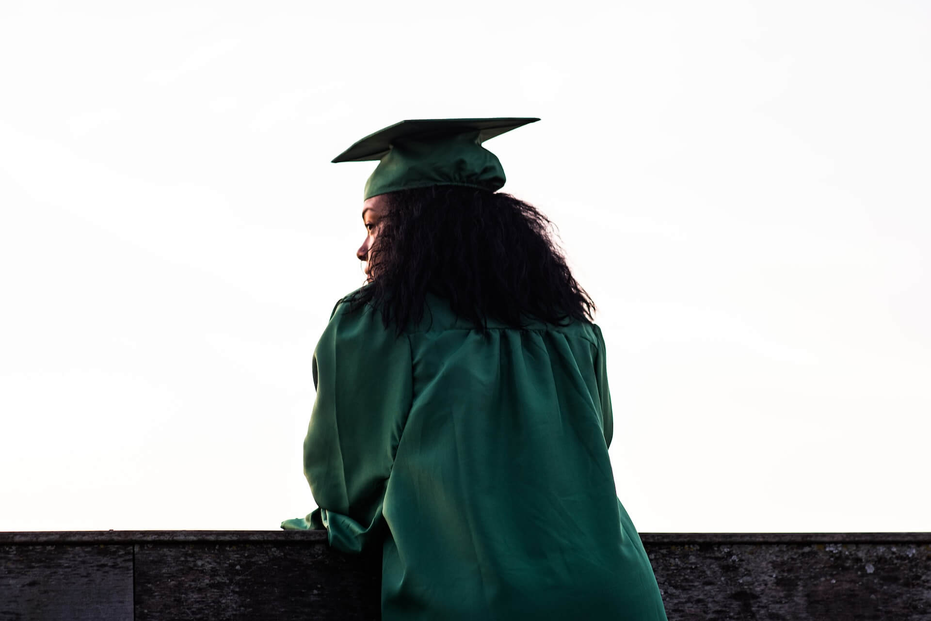 student in graduation gown leaning on ledge