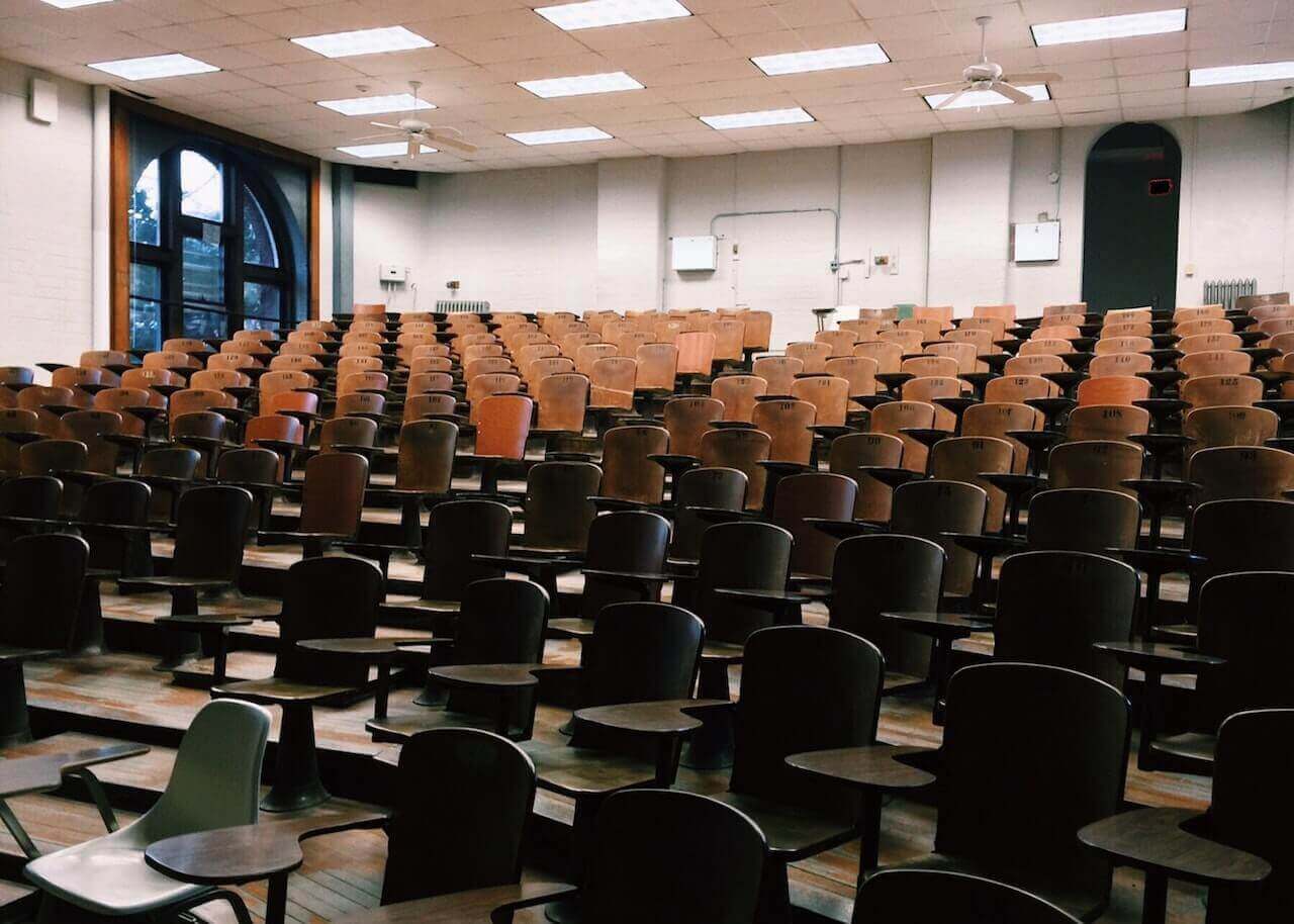 An empty college lecture hall, with many seats and desks.