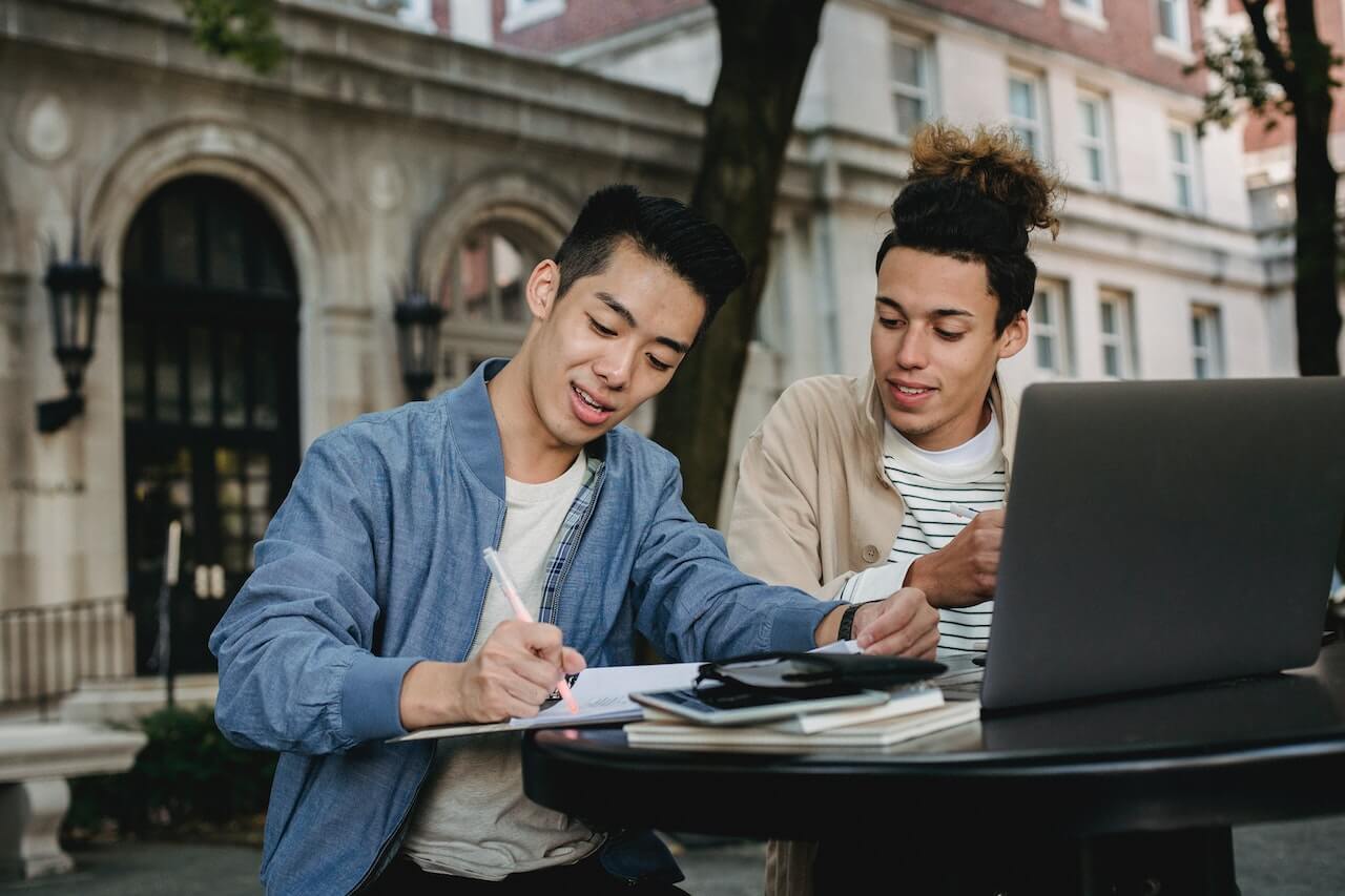 Two students studying at a table with computers and notebooks