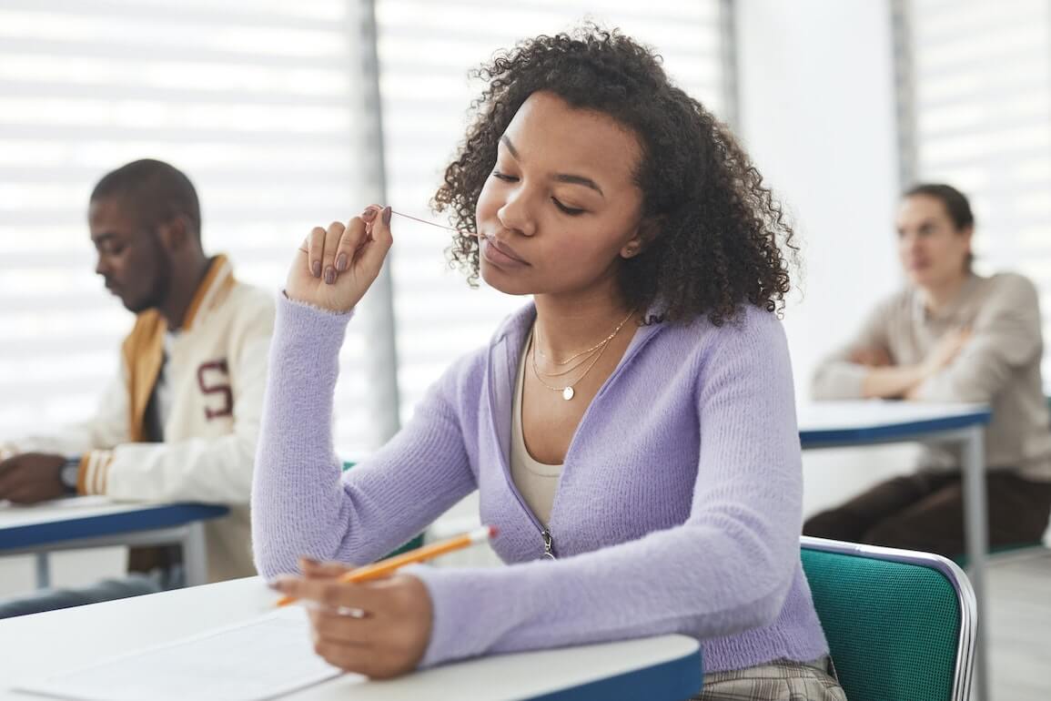 Girl in purple sweater taking a test and chewing gum.