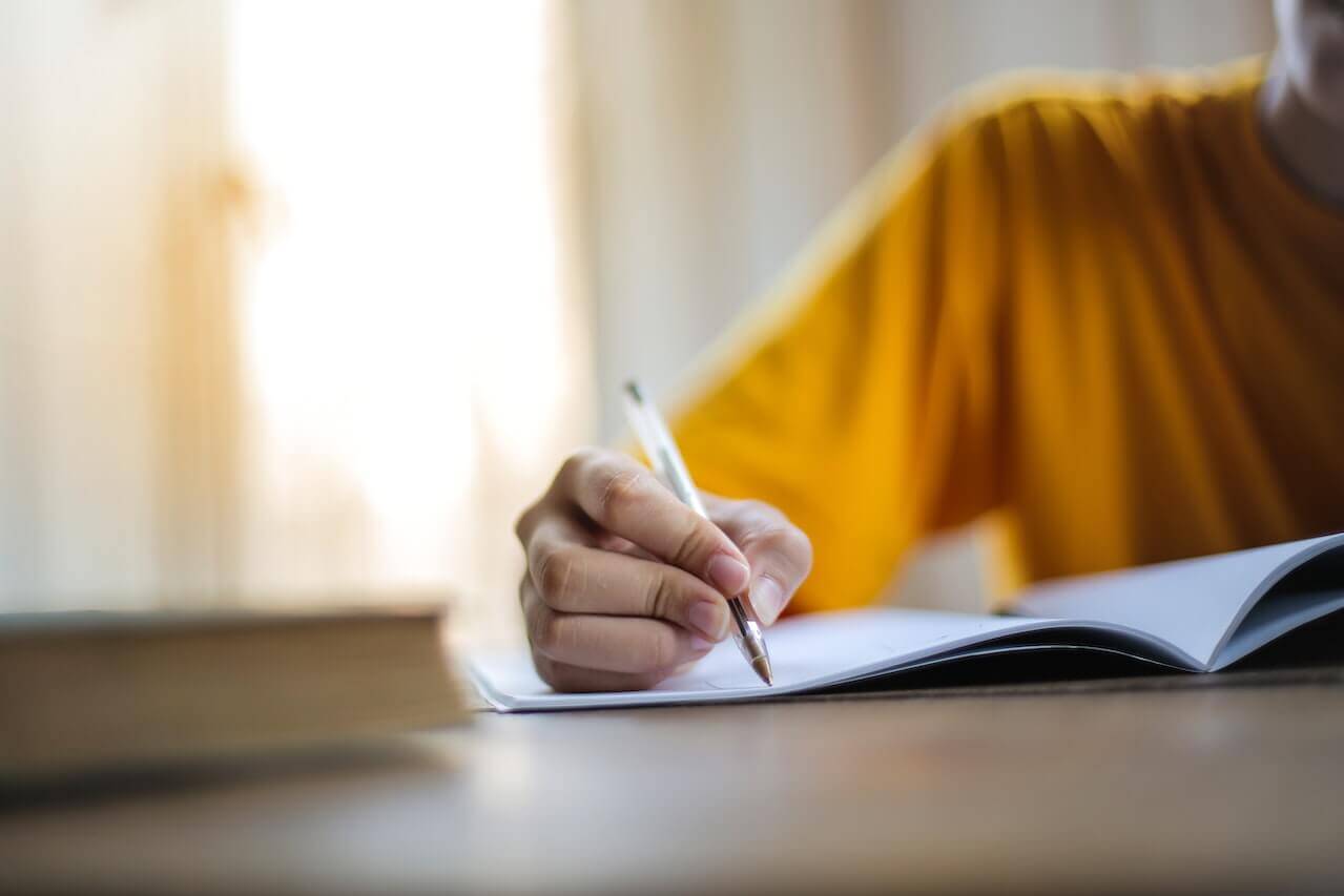 A person writes in pen on notebook paper.