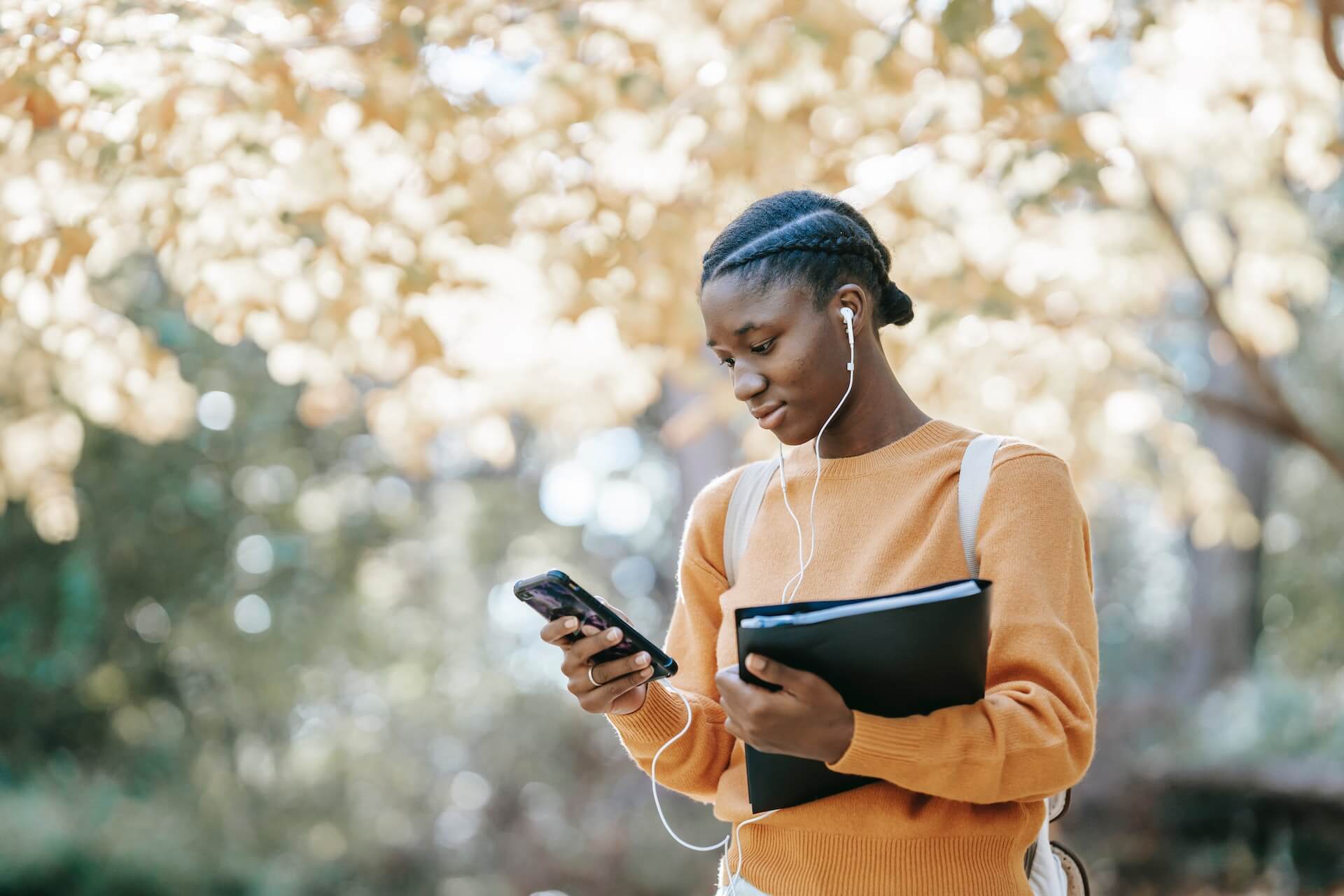 Female student walking through campus listening to music and carrying a folder