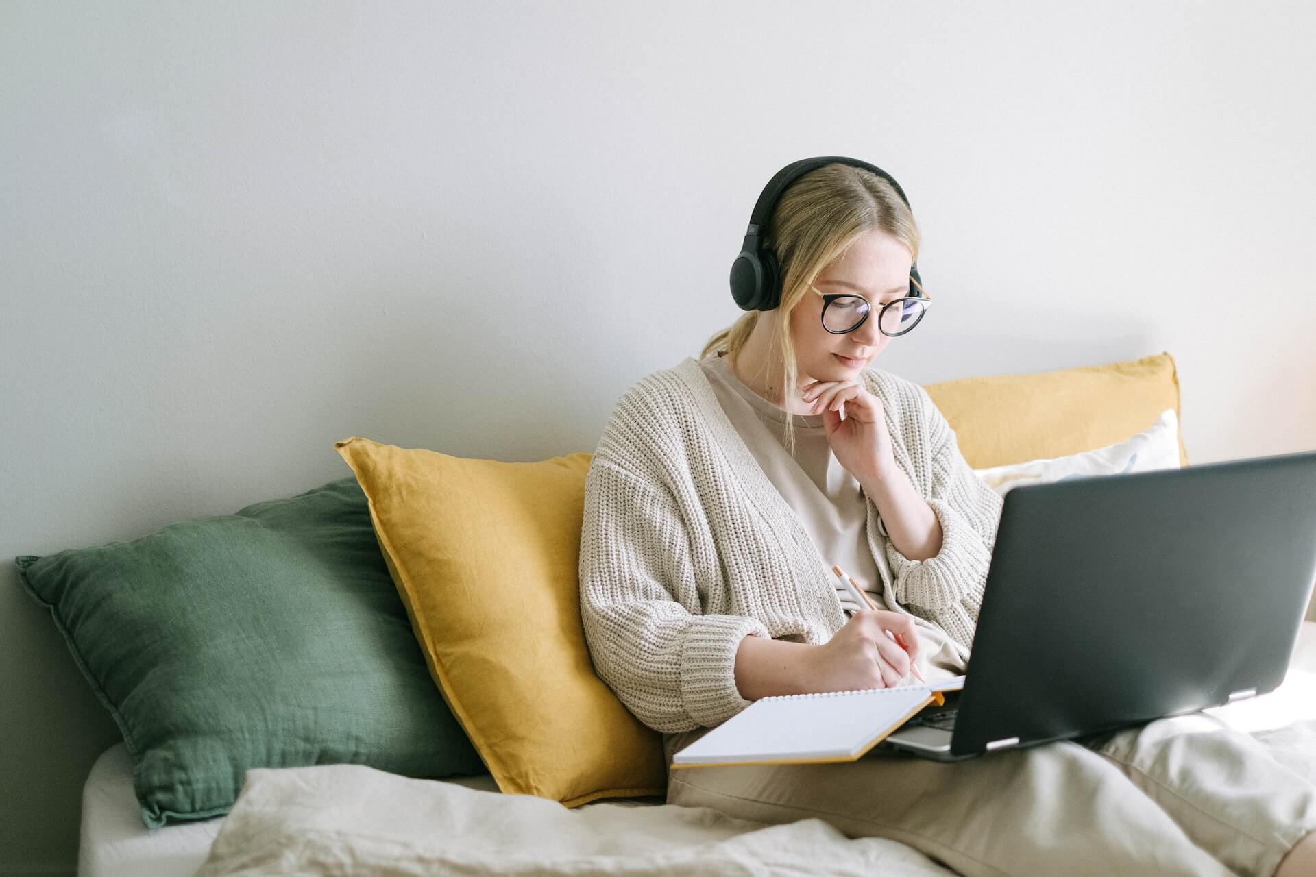 Student writing in a notebook and reading a laptop in bed