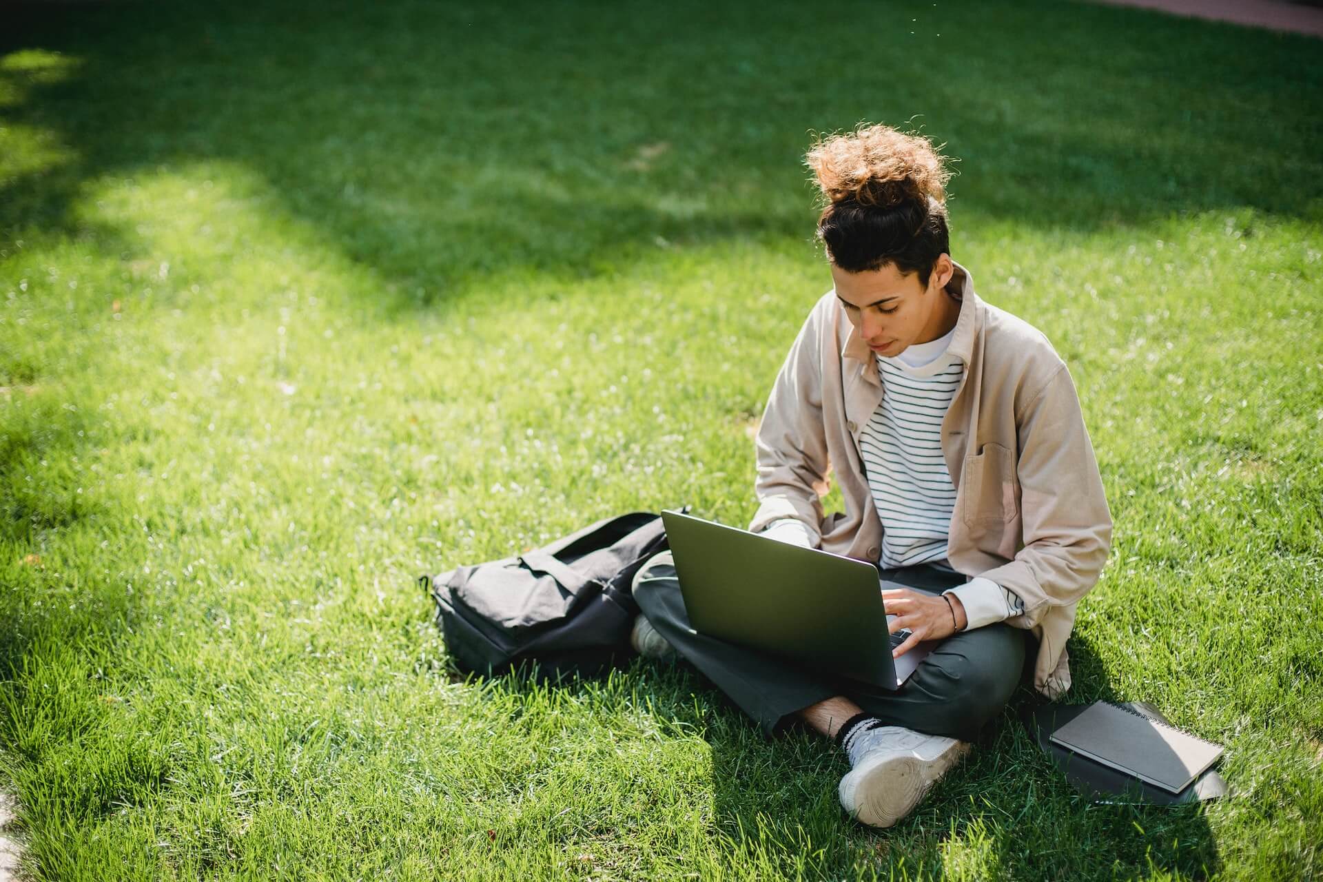 College student sitting on the lawn and looking at his laptop