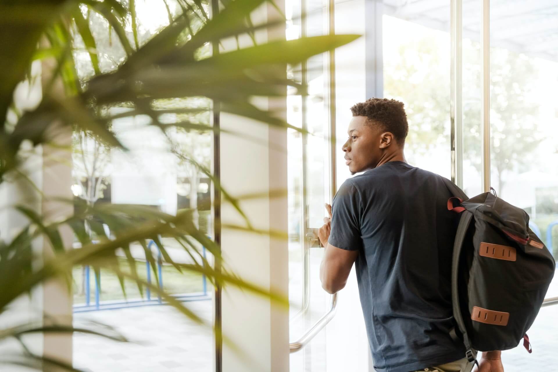 Male student stepping outside carrying a backpack