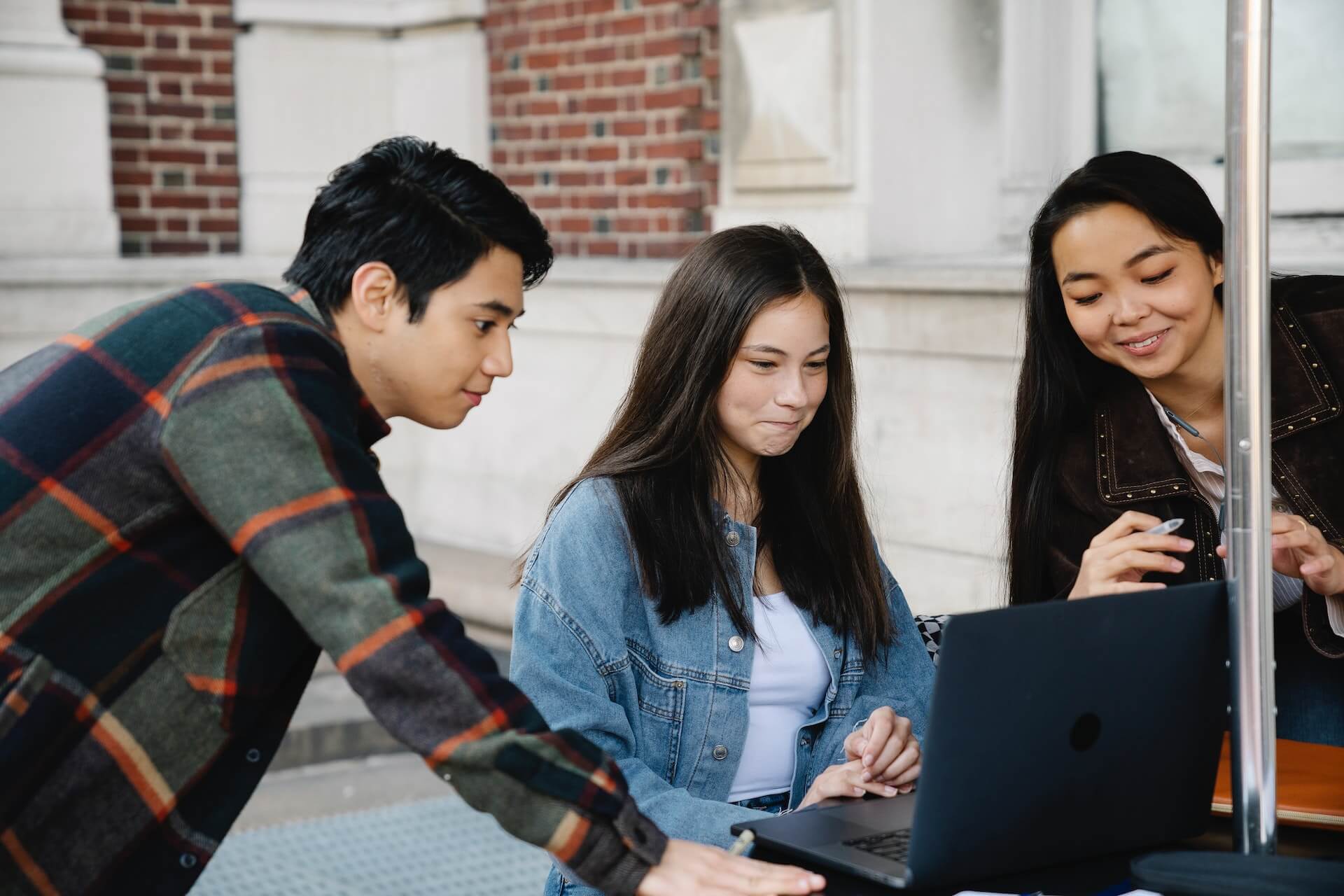 Three students working on a laptop on a table outside