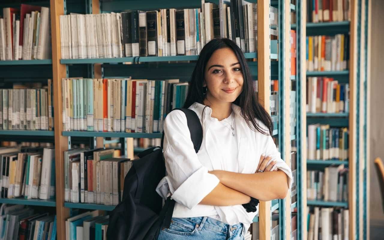 female student leaning on bookshelf in library