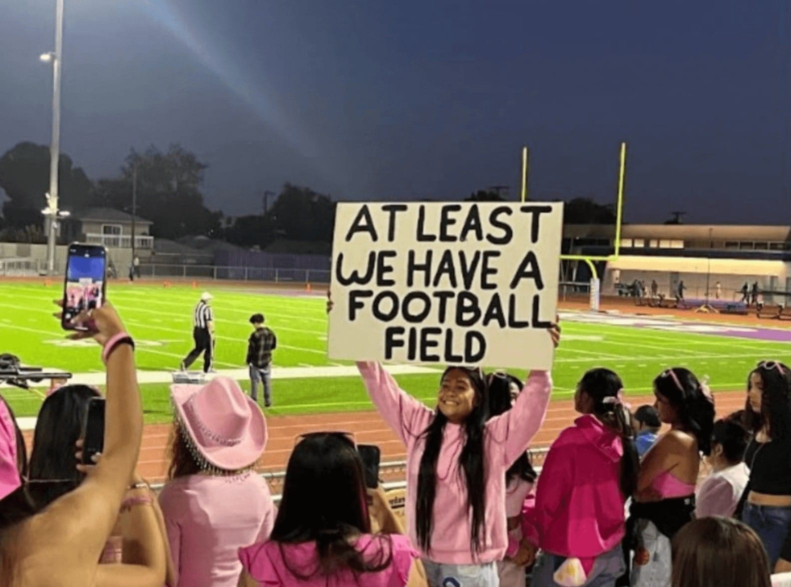 girl holding up sign that reads 'at least we have a football field'