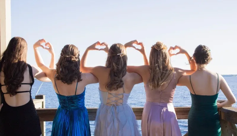 five graduates pose and make heart shape with hands