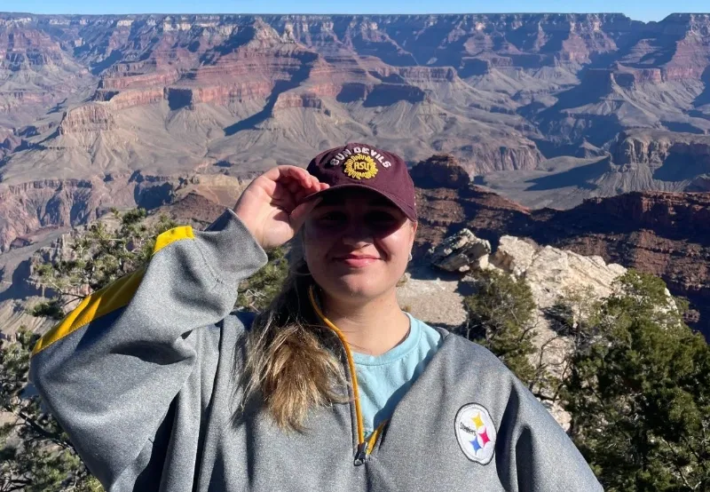 student with cap stands in front of canyon on spring break trip