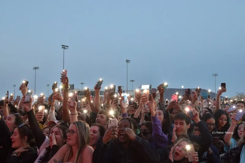 students wave phone flashlights at an outdoor concert