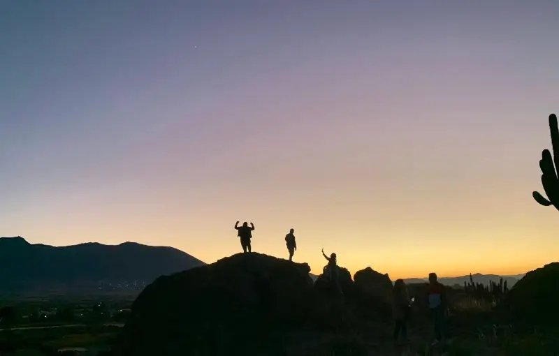 students stand on a rock as the sun sets