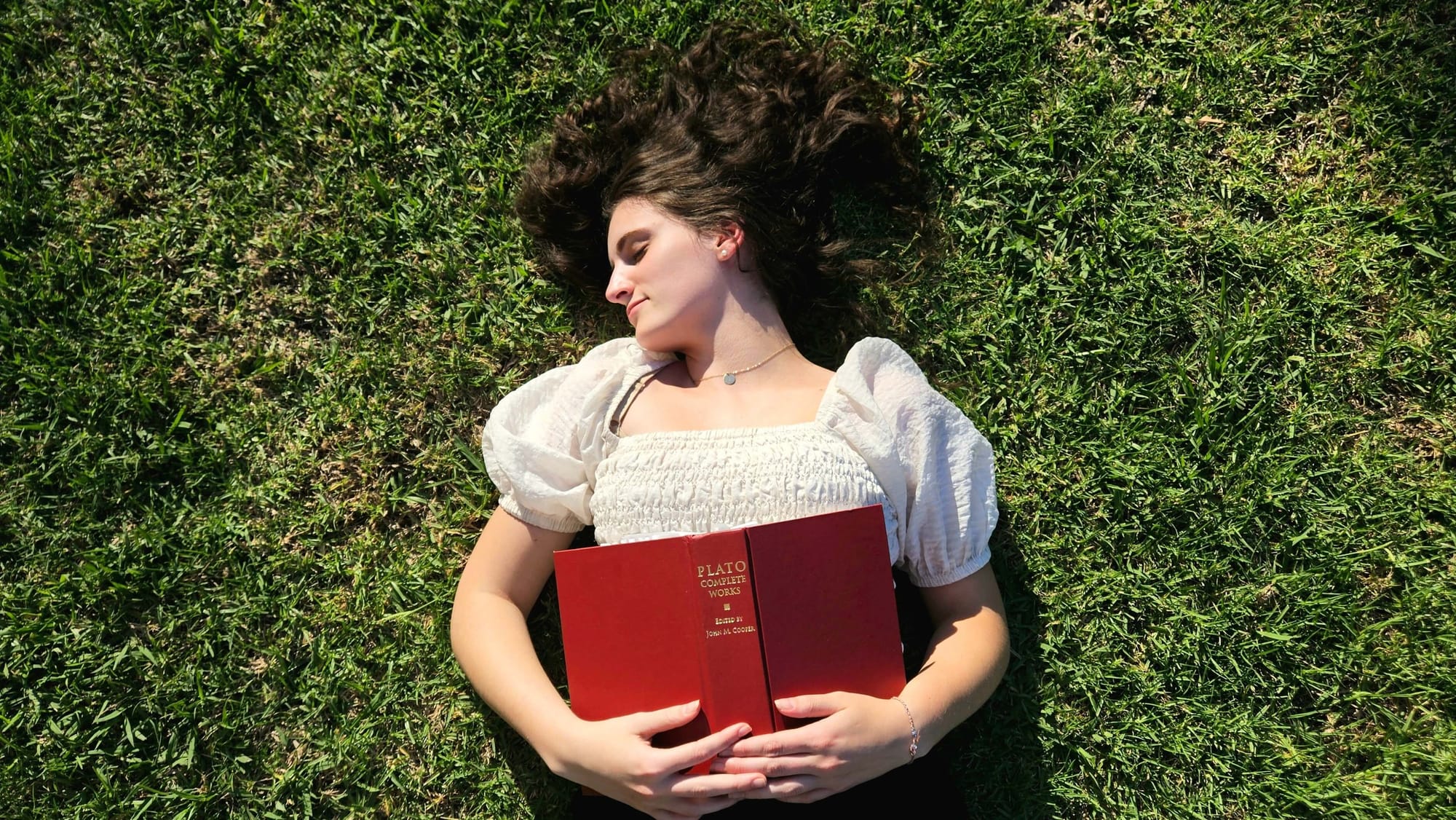 woman lies in the grass with a book on philosophy