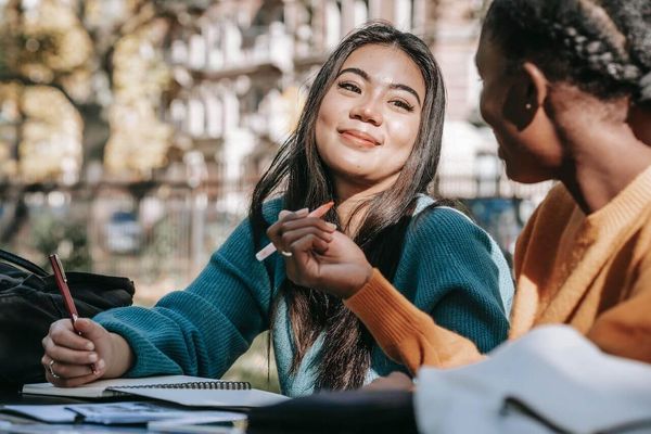 Two female college students work together, writing at a table outdoors.